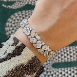 A close-up of a wrist adorned with the Cluster Diamond Evening Bracelet, featuring sparkling oval and round stones in 18k white gold, paired with a sequined sleeve against a green and white geometric background.