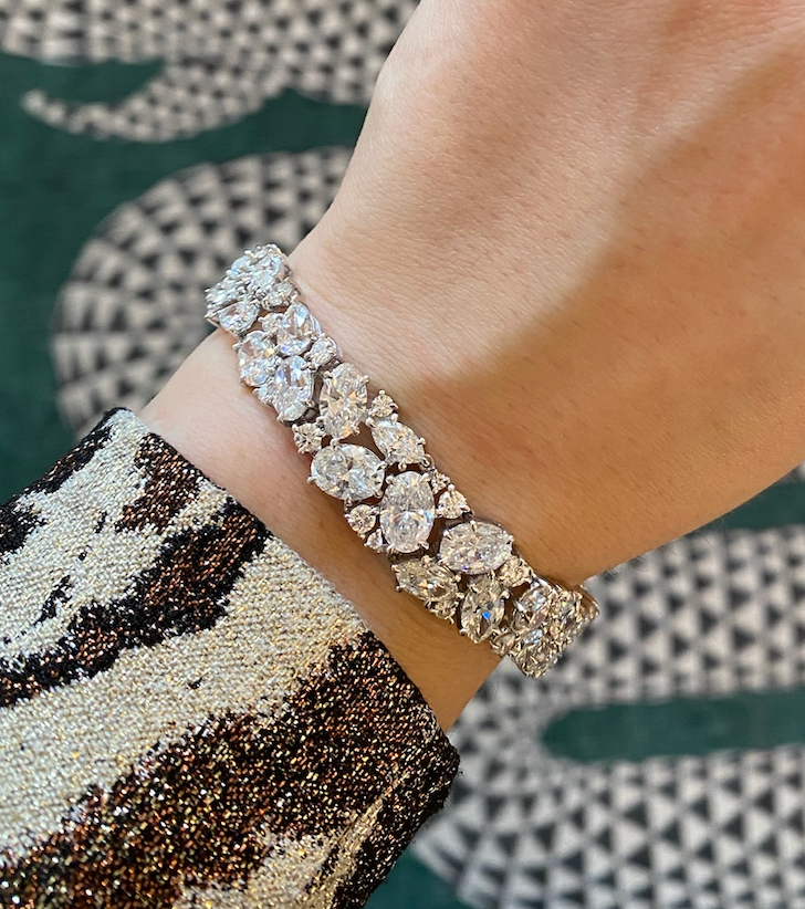 A close-up of a wrist adorned with the Cluster Diamond Evening Bracelet, featuring sparkling oval and round stones in 18k white gold, paired with a sequined sleeve against a green and white geometric background.