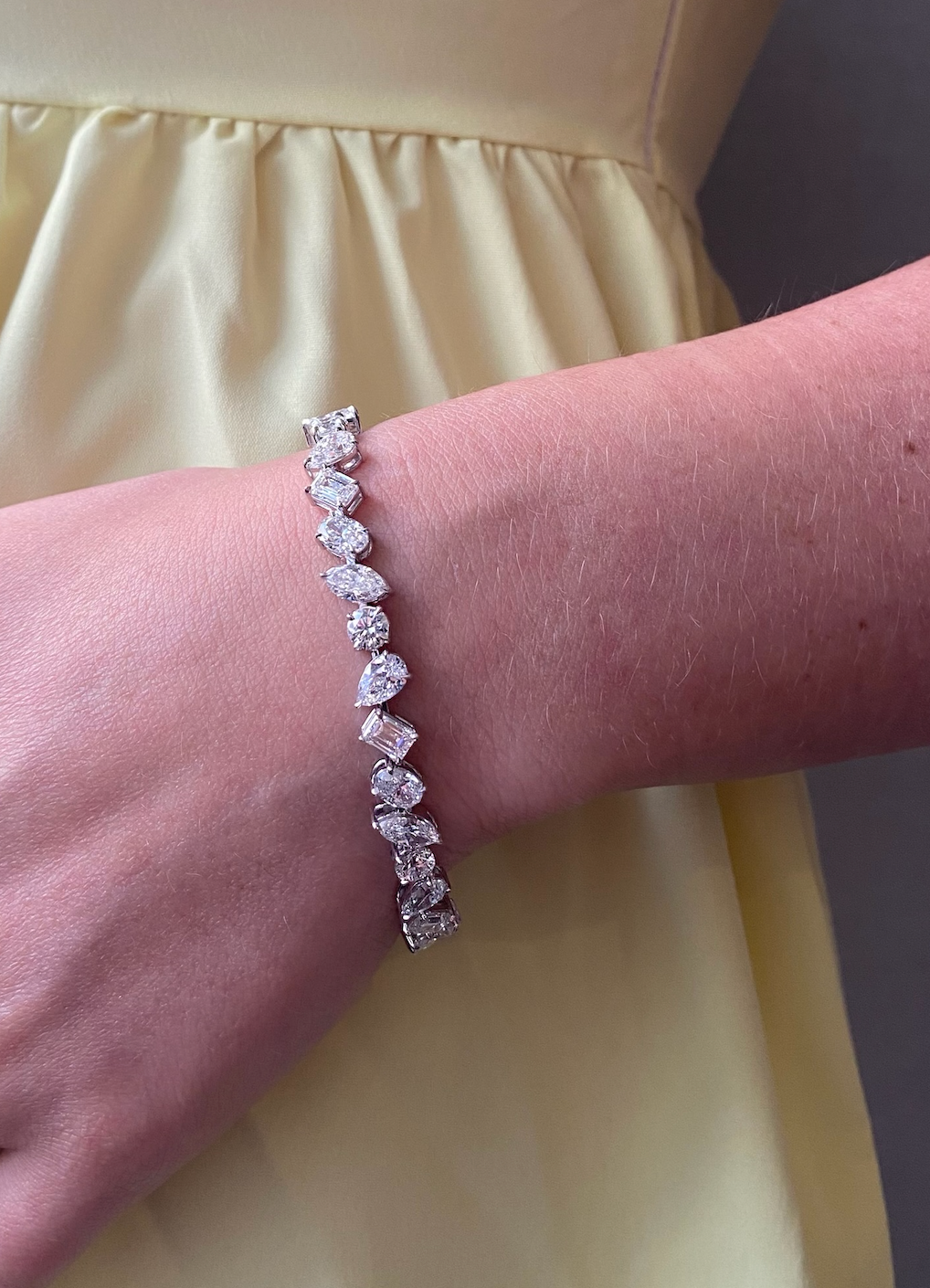 A close-up of a wrist adorned with the Mixed Shape Diamond Tennis Bracelet in 18k gold, sparkling against a yellow dress background.
