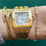 A wrist adorned with a gold Cartier watch with a square face and Roman numerals, an 18k gold nail-shaped bracelet with a diamond, and the Serpentine Station Bracelet with Hexagon Diamond Trios.