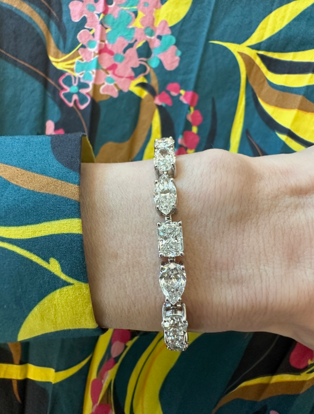 A hand adorned with the Medium East-West Mixed Shape Diamond Tennis Bracelet in 18k white gold rests on colorful, patterned fabric with blue, yellow, and pink designs.