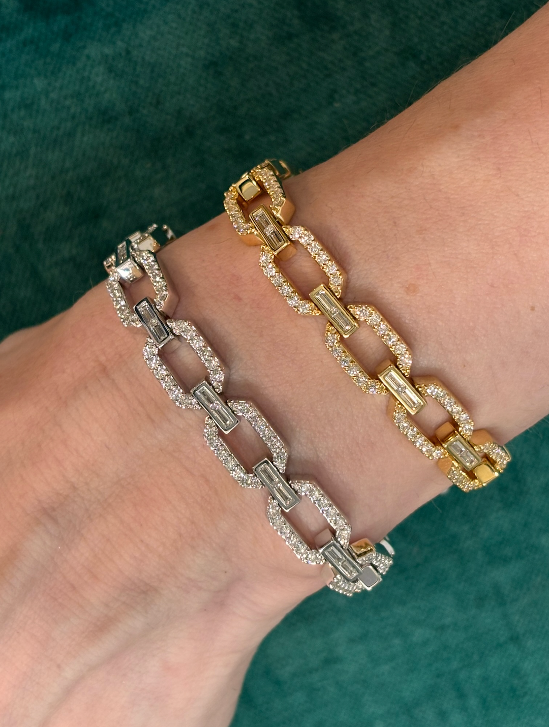 A wrist adorned with the Bezel Set Baguette Diamond Pavé Chain Bracelet in white gold, encrusted with sparkling gems and baguette diamonds, glimmers elegantly against a green textured background.