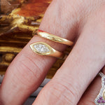A hand displays two gold rings on the ring finger—an 18k yellow gold band and a marquise diamond ring set horizontally. A Serpent Wraparound Ring with Marquise Diamond in silver is partly visible on the pinky finger.
