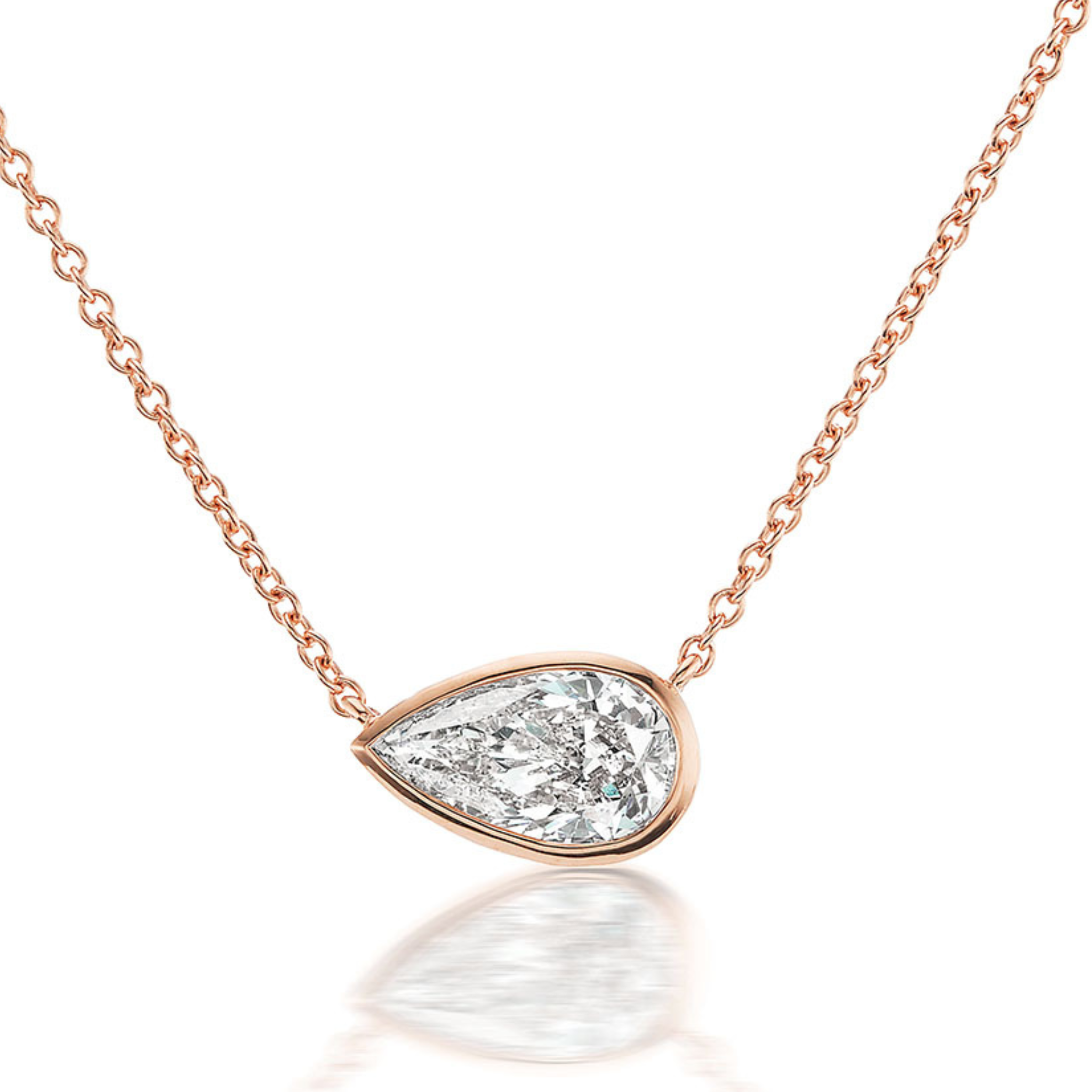 The Small East-West Bezel Set Pear Diamond Pendant in Rose Gold features a dazzling pear diamond in an 18K rose gold bezel, showcased on a delicate chain against a white background.