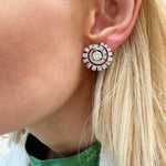 Close-up of a woman's ear wearing Celestial Swirl Ear Jackets in white gold with mixed shape diamonds. She has straight blonde hair and is styled in a green top and white jacket.