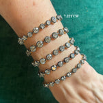 A wrist is adorned with five dazzling Collet Set Round Diamond Bracelets in black rhodium, their round diamonds sparkling beautifully against a green textured backdrop. Text on the image reads 7.22 TCW.