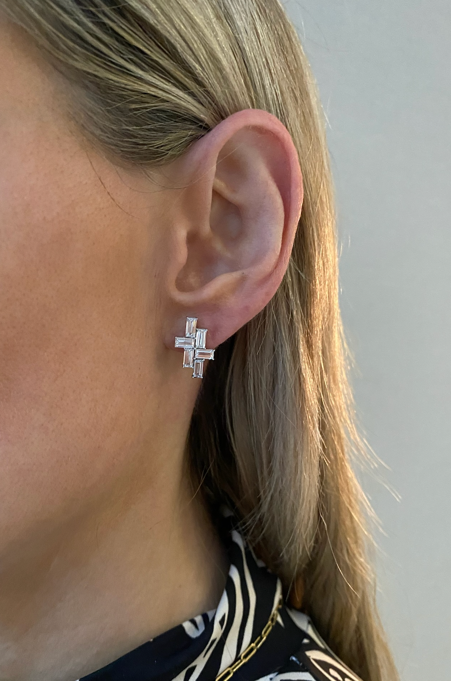 Close-up of a woman's ear wearing Tetris Studs with Baguette Diamonds in White Gold. She has light blonde hair and is dressed in a black and white patterned top.