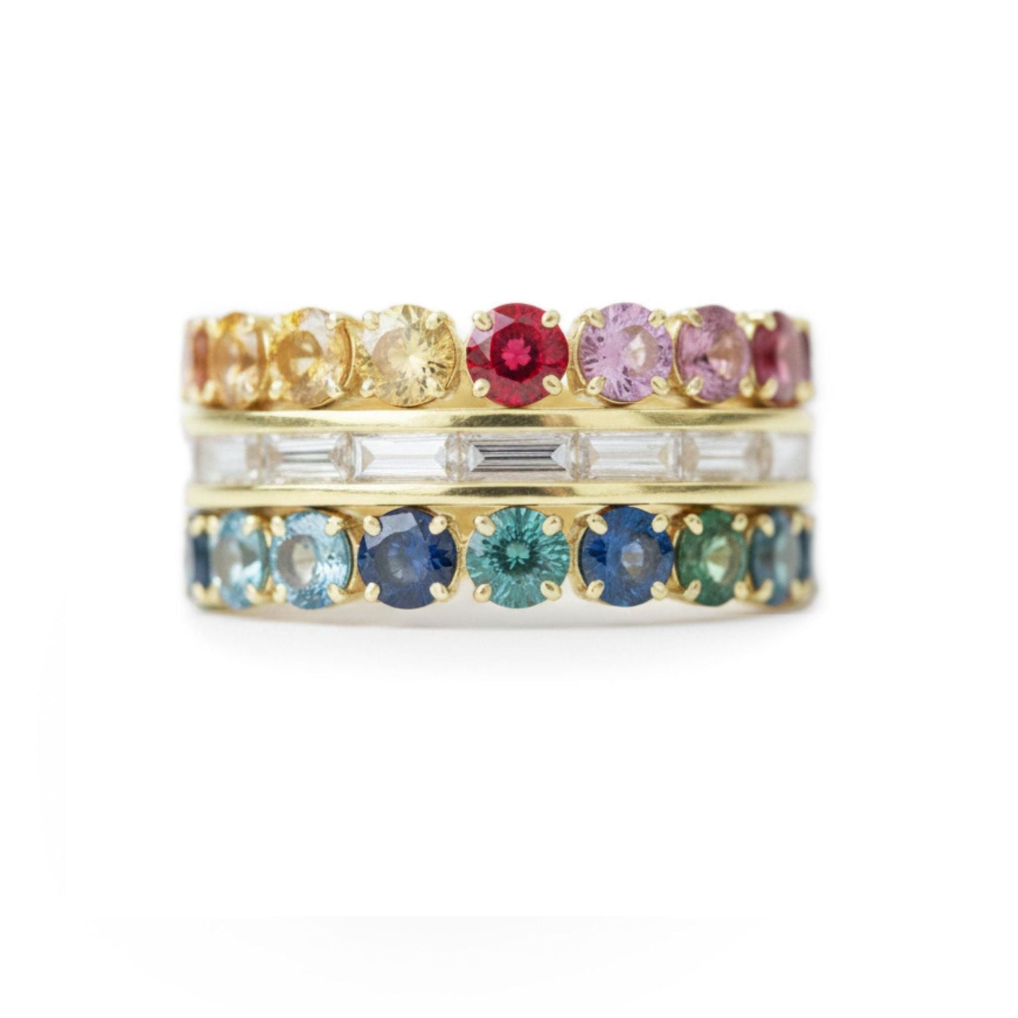 The Channel Set Baguette Diamond Engagement Ring features stacked yellow gold bands with round multicolor sapphires on top, rectangular clear stones in the center, and round blue and green gems below, shown on a white background.