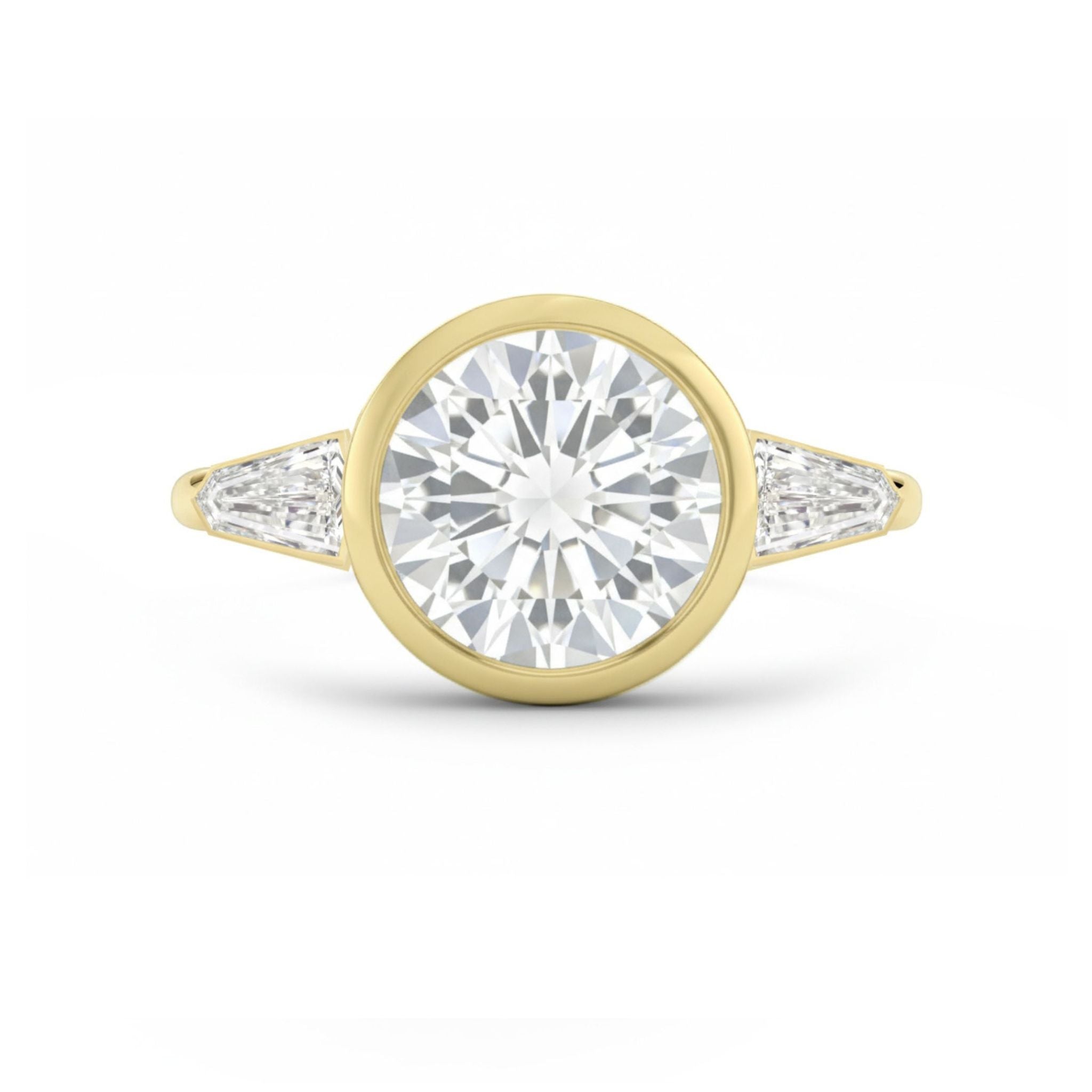 The Bezel Set Round Diamond Engagement Ring with Tapered Baguette Side Stones in Yellow Gold features a polished band, a large round bezel-set diamond center, and two tapered baguette diamonds on each side.