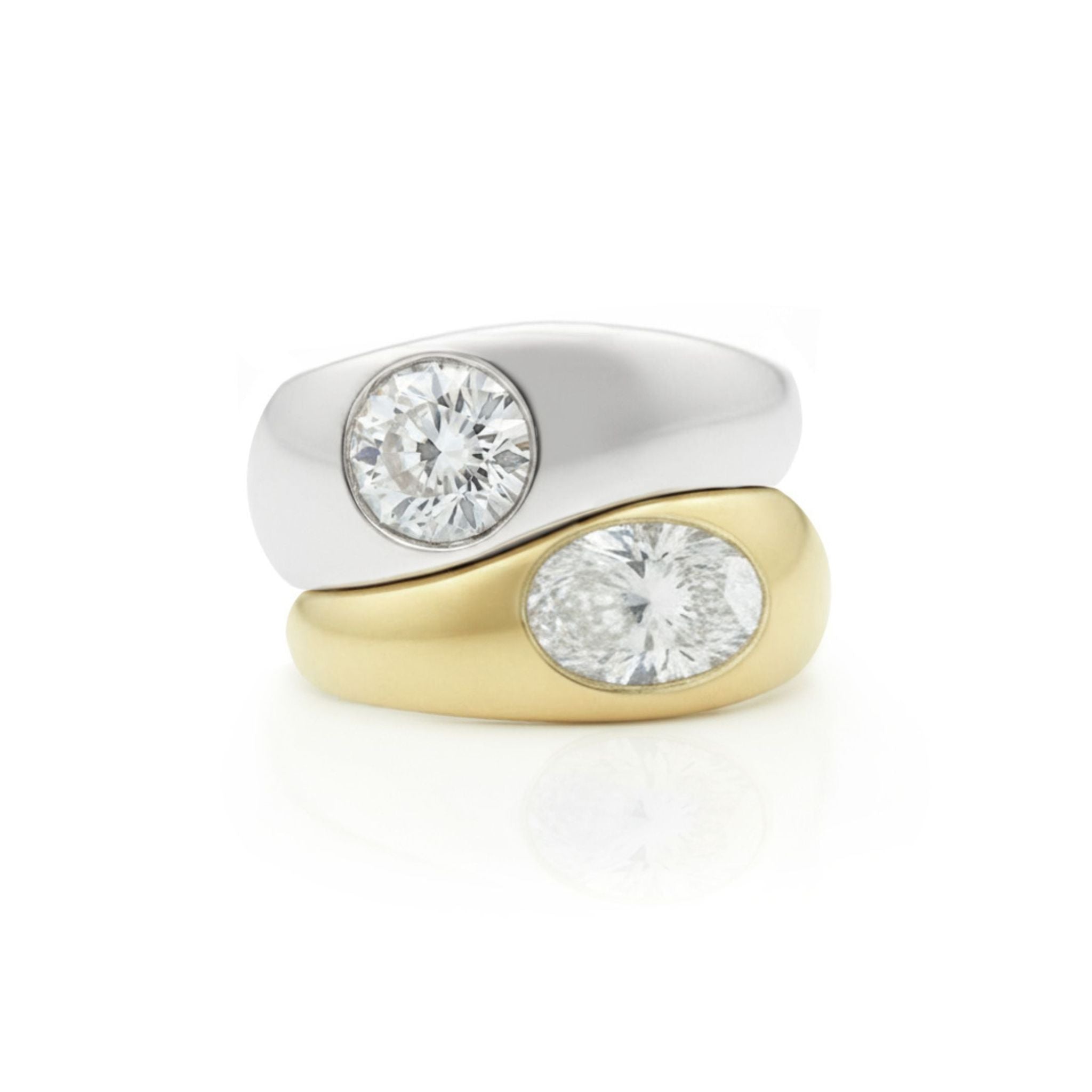 A Stacked Burnish Set Round Diamond in White Gold and an Oval Shape Diamond in Yellow Gold Engagement Ring are paired together against a white background.