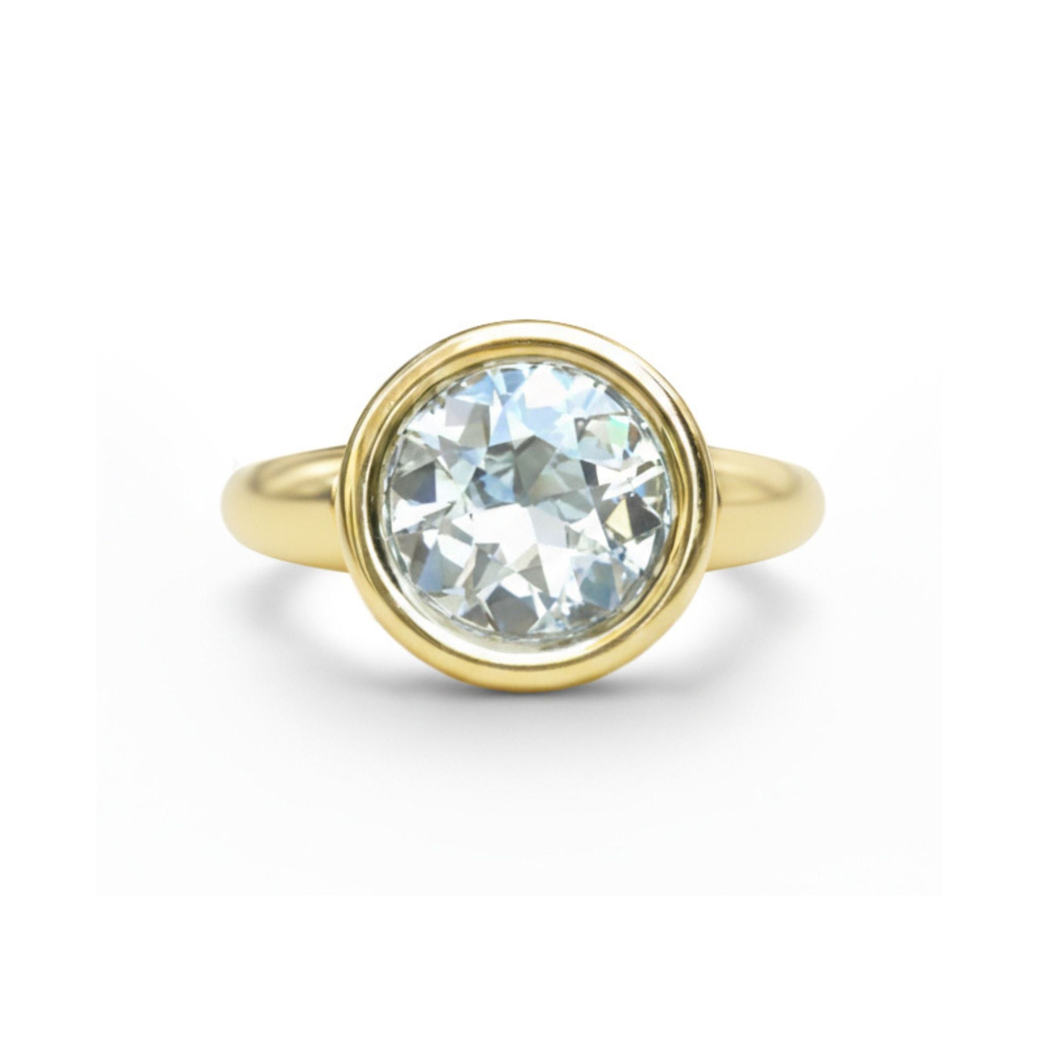 The Bezel Set Round Diamond Engagement Ring in Yellow Gold features a large, clear round diamond in a simple bezel setting, displayed against a white background.