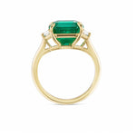 The Emerald Cut Emerald Engagement Ring in Yellow Gold features a center emerald with two trapezoid baguette diamond side stones, shown from the side against a white background.