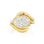Introducing the Asymmetrical Wave Ring Jacket with Birthstone Accents in Yellow Gold: a stunning double band ring crafted from 18k yellow gold, featuring wavy bands adorned with a large oval diamond at the center and highlighted by a small blue birthstone and a delicate white diamond accent on one side.