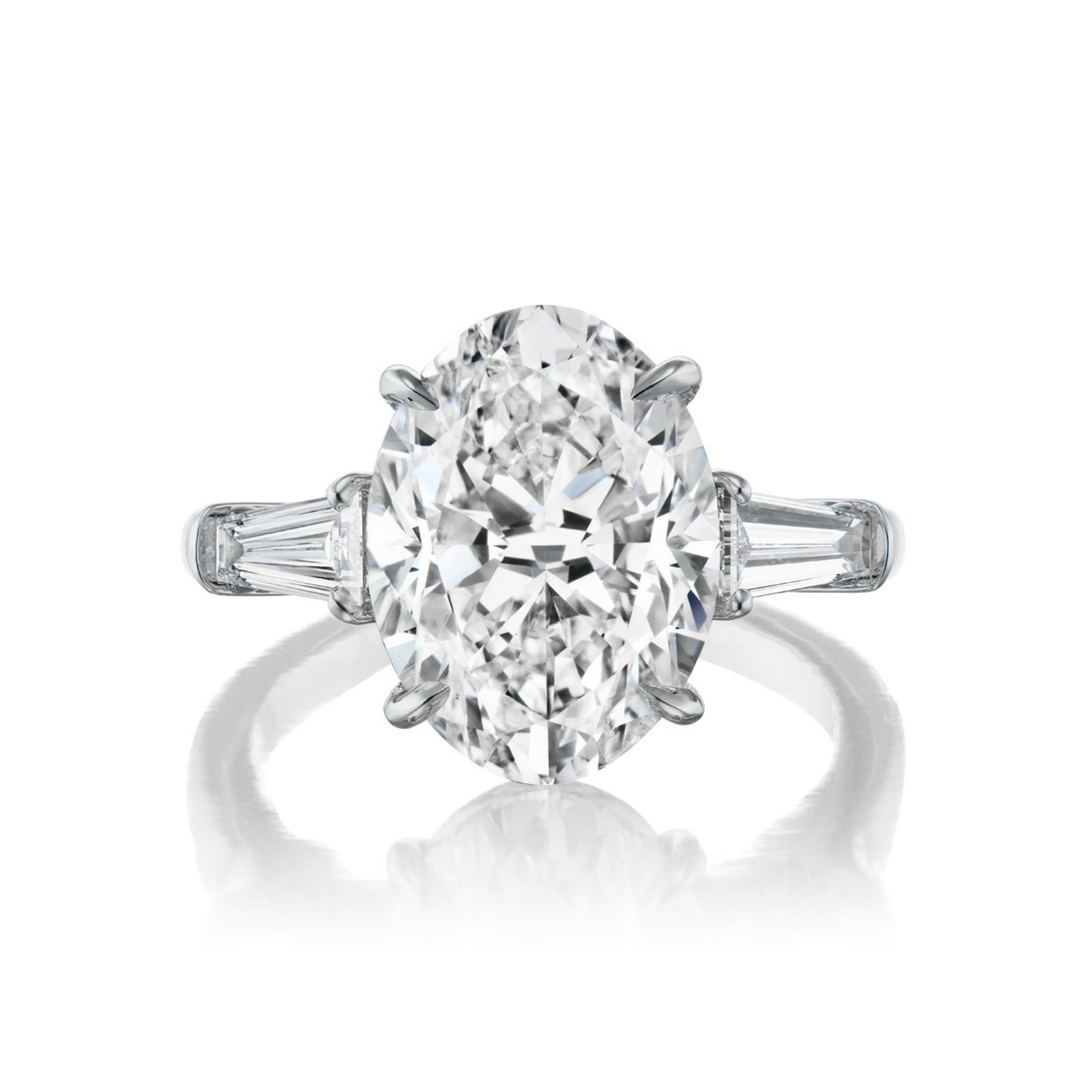 The Oval Diamond Engagement Ring with Tapered Baguette Side Stones features an elegant oval-cut center diamond flanked by tapered baguette side stones, all set on a polished platinum band and showcased against a white background.