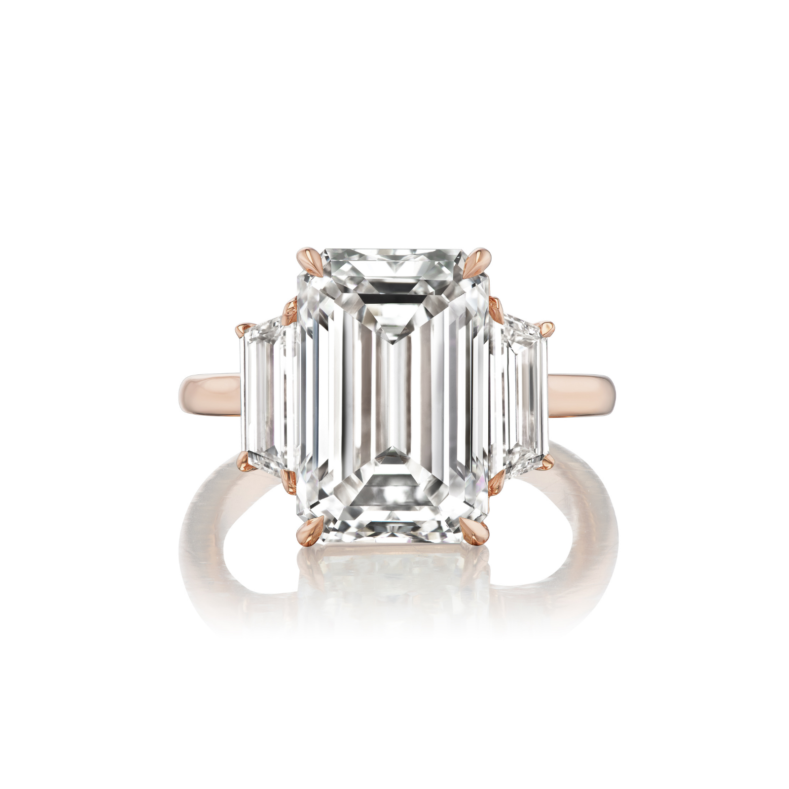 The Emerald Cut Diamond Engagement Ring with Trapezoid Side Stones features a large emerald-cut diamond at the center, flanked by two smaller trapezoid diamonds on each side, and is shown in elegant rose gold against a white background.