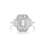 Introducing our Half Bezel Set Three Stone Engagement Ring, showcasing a stunning emerald-cut diamond at the center, flanked by trapezoid side stones and elegantly set on a slim platinum band.