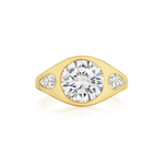 A Burnish Set Gypsy Ring with Round and Pear Shape Diamonds in Yellow Gold by Serpentine Jewels is displayed on a white background. This exquisite ring features a large round central diamond accented by pear-shaped diamonds on either side, embodying timeless elegance and classic sophistication.