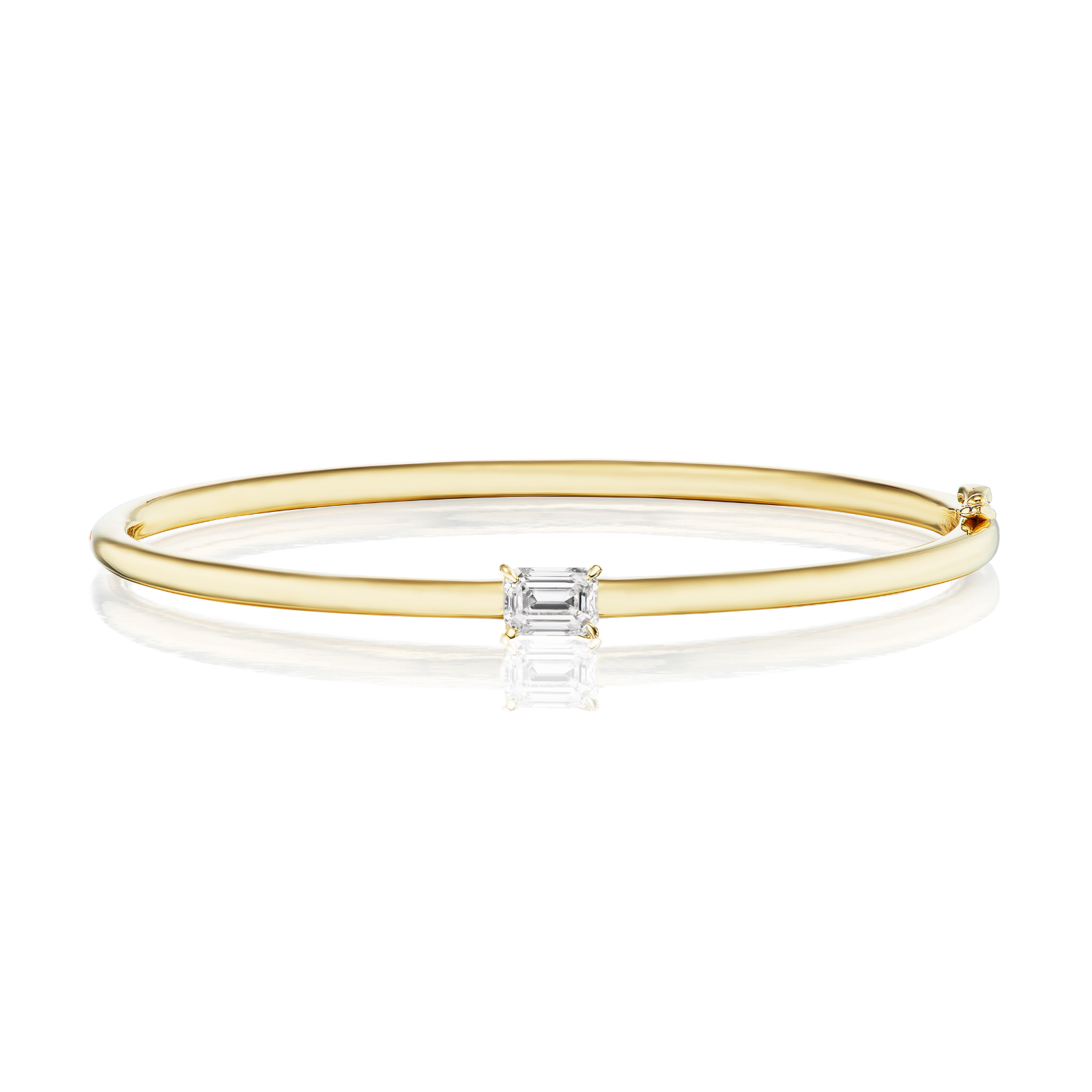The East-West Set Emerald Cut Diamond Bangle is a slender bracelet crafted from 18K white gold, showcasing a centrally set emerald cut diamond of VS2 clarity, presented against a white background.