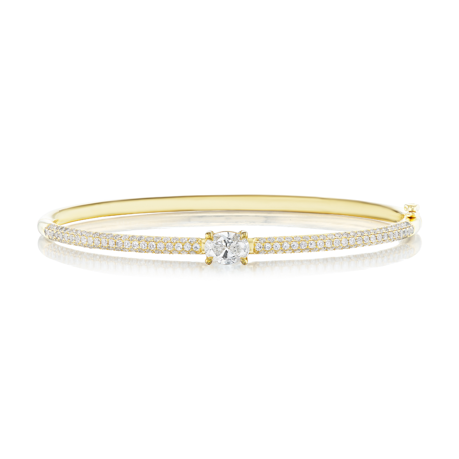 The East-West Set Oval Shape Diamond Pavé Bangle features an elegant 18k gold design with a central oval-shaped diamond and two rows of pavé diamonds along the band, displayed on a white background.