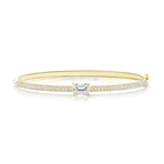 The East-West Set Emerald Cut Diamond Pavé Bangle is a stunning 18k gold bangle bracelet featuring a central emerald-cut diamond and two rows of small round diamonds along the band, displayed on a white background.