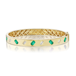 The Alternating Emerald Cut Diamond and Emerald Bangle in Yellow Gold features luxurious 18K yellow gold with alternating emerald-cut green stones and white rectangular accents, a lattice interior design, and is displayed on a white reflective surface.