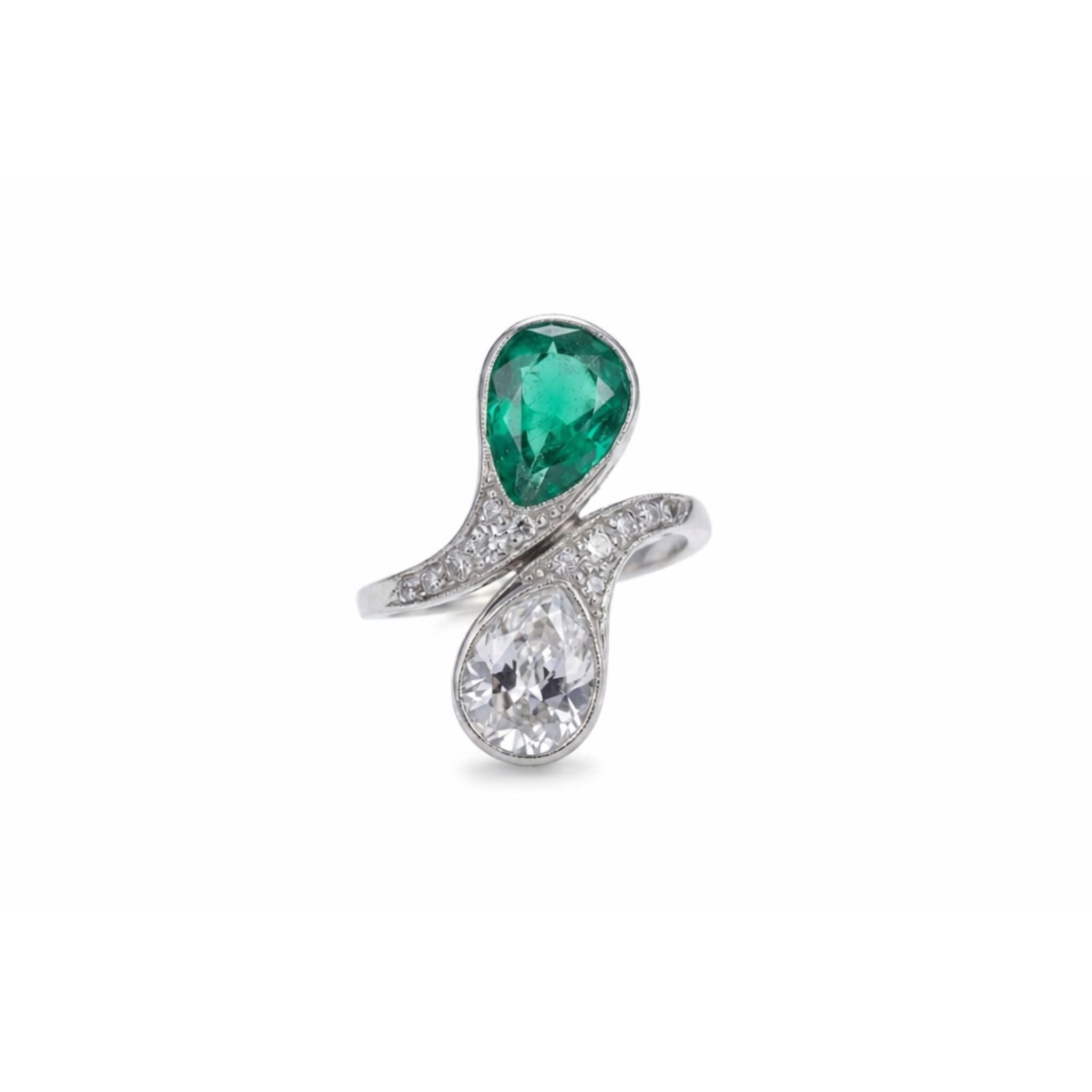 The Emerald and Diamond Bypass Ring features a stylish platinum band with a bypass design, showcasing a pear-shaped emerald and a pear-shaped white diamond, both accented by pavé-set diamonds.