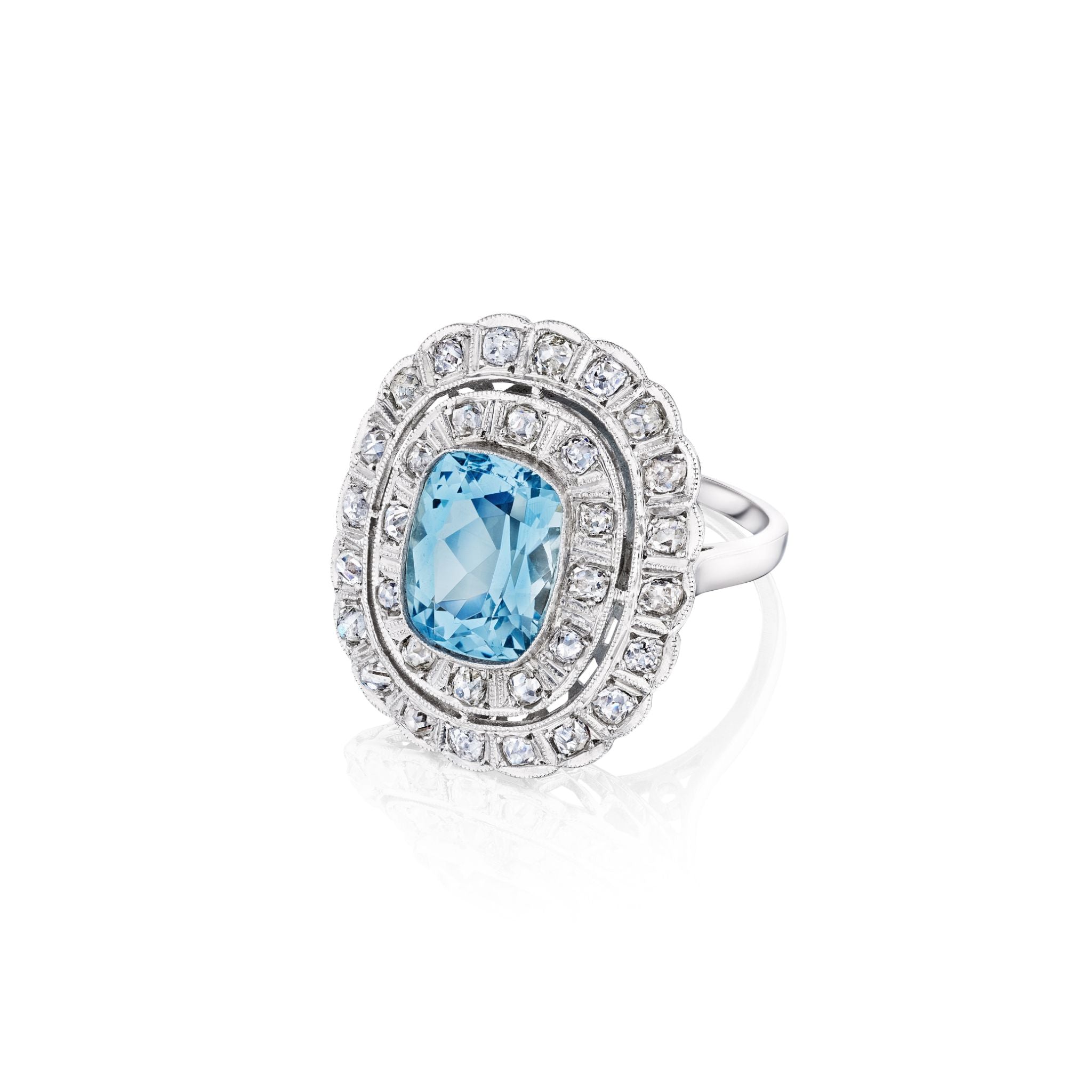 The Aquamarine and Diamond Ring showcases a large oval blue gemstone at the center, encircled by two rows of small round diamonds in a decorative halo setting, shown against a white background.