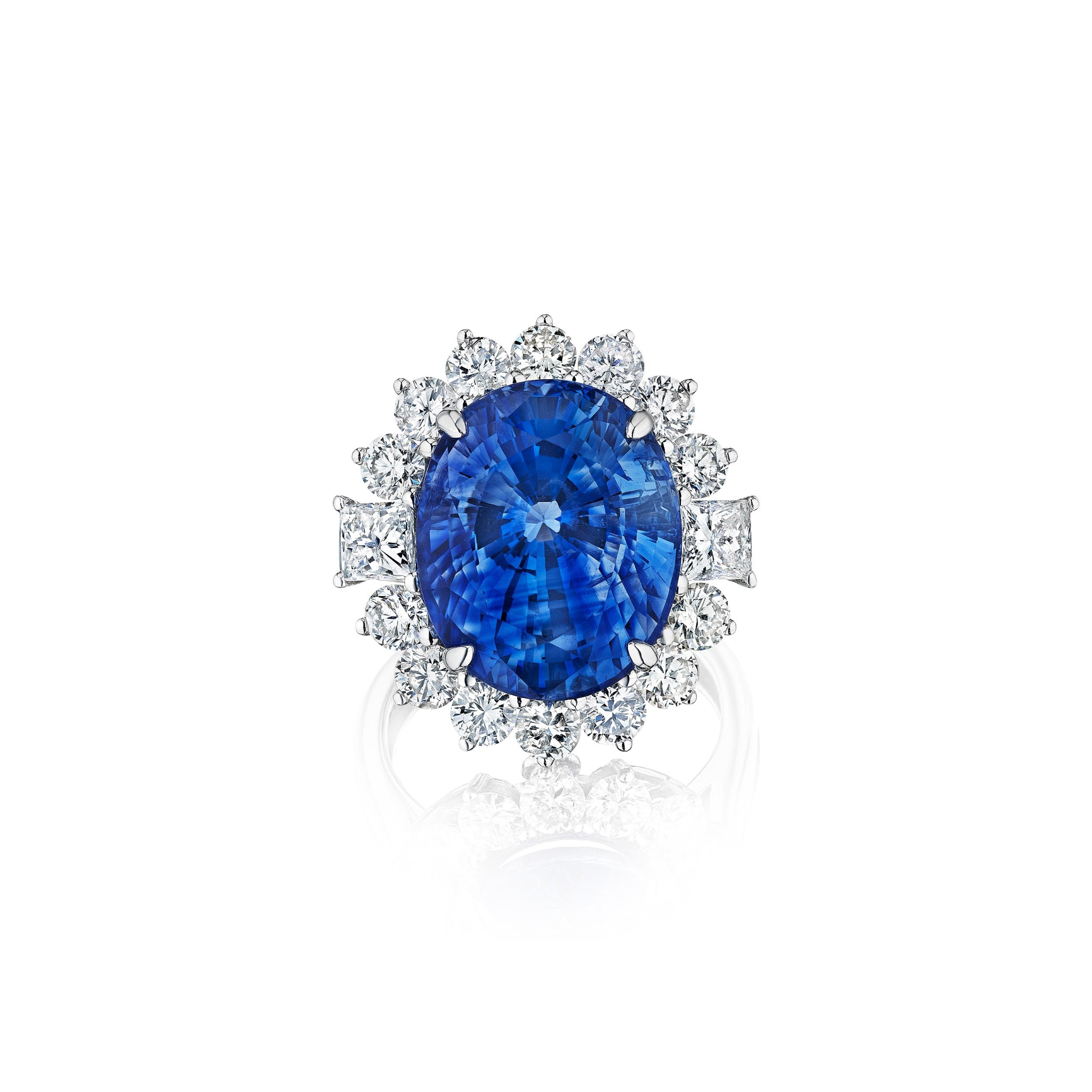 The Sapphire and Diamond Ring features an 18k white gold band set with a large oval Ceylon sapphire at the center, encircled by sparkling white diamonds in a delicate floral halo design.