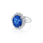 The Vintage Sapphire and Diamond Ring showcases a luxurious large oval Ceylon sapphire, elegantly framed by sparkling round and pear-shaped diamonds, all set in radiant 18k white gold and presented against a white background.
