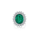 The Vintage Emerald and Diamond Ring, featuring an oval green Colombian emerald encircled by two rows of round white diamonds and set in an 18K white gold band, is elegantly displayed on a plain white background.