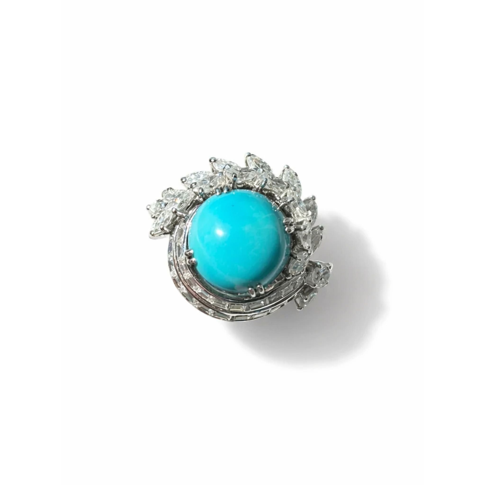 The Turquoise and Diamond Ring features a large round turquoise cabochon at the center, framed by a fan of marquise and round diamonds, set in platinum and displayed on a white background.
