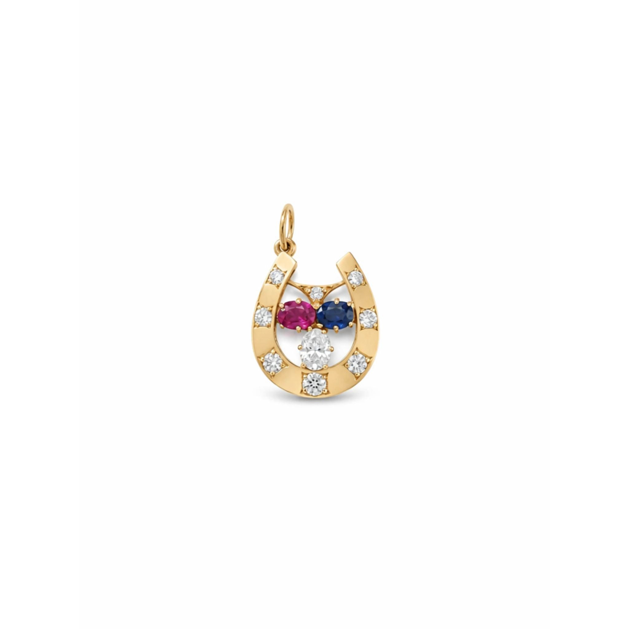The Sapphire, Ruby and Diamond Pendant features an 18K gold horseshoe design with small diamonds along the curve, accented by a central sapphire, ruby, and clear gemstone. A small top loop allows easy attachment to your favorite chain.