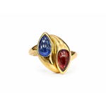 Bulgari Pink Tourmaline and Sapphire Ring, circa 1980: A gold ring featuring two marquise-shaped cabochon gemstones—one vivid blue sapphire and one striking pink tourmaline—set side by side in a modern, sculptural design reminiscent of classic Bulgari style, displayed against a white background.
