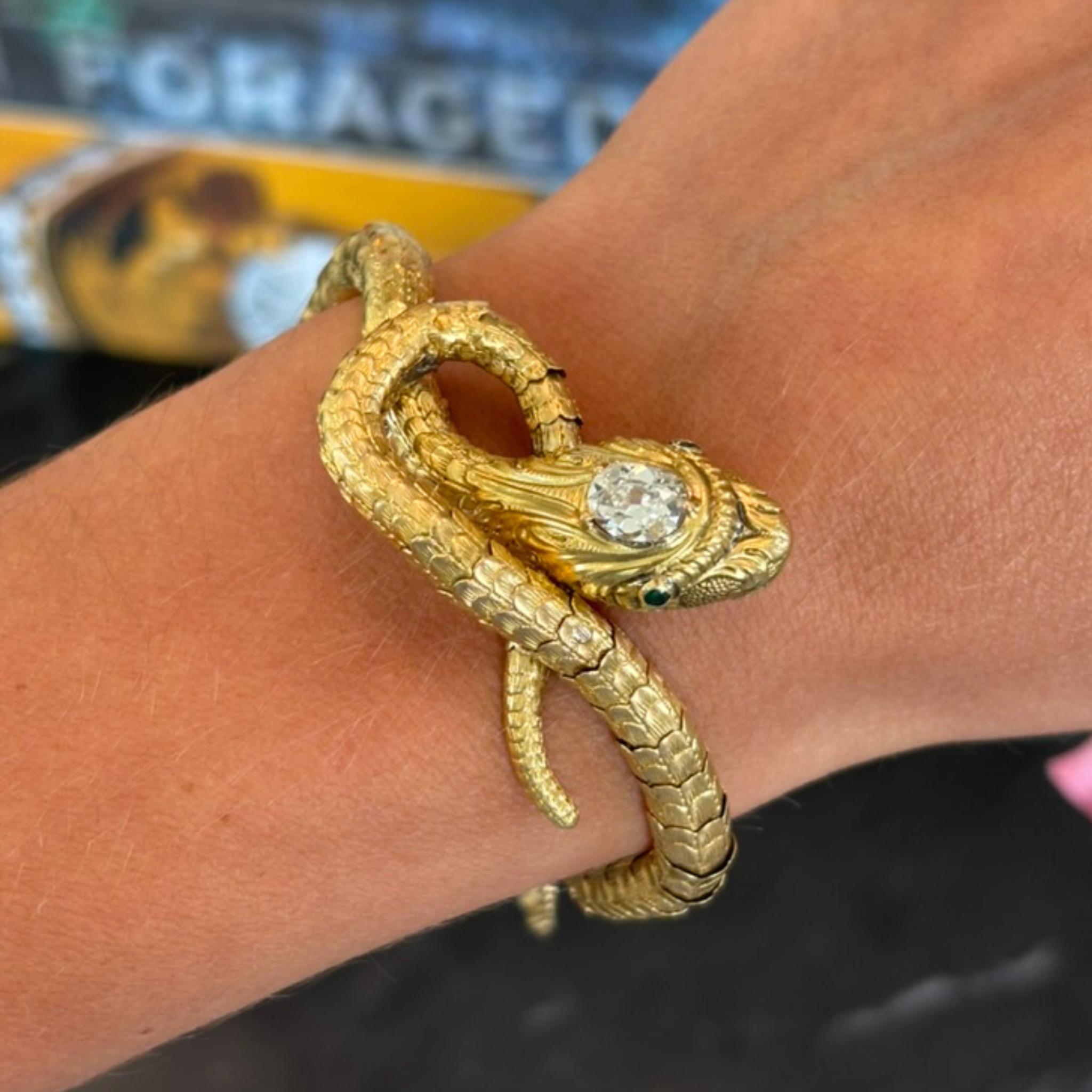 The Antique Gold, Diamond and Emerald Bracelet features a coiled snake design with emerald eyes and a large diamond on its head, elegantly wrapping around the wrist.