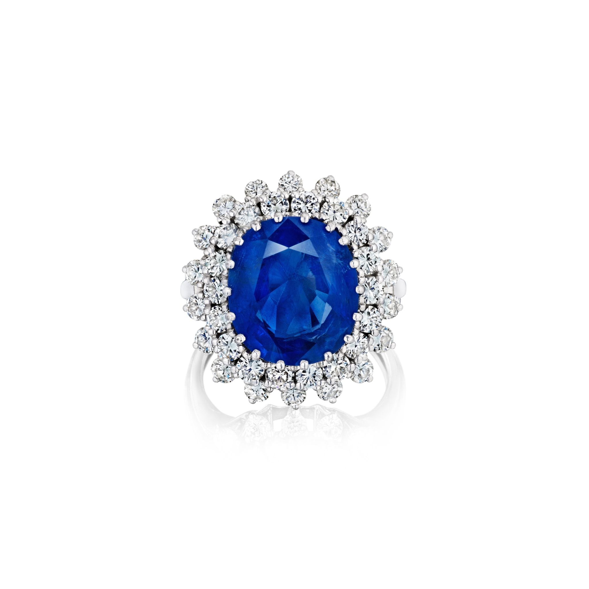 The Sapphire and Diamond Ring showcases a large cushion-cut blue Burmese sapphire encircled by round white diamonds, all set against a white background.