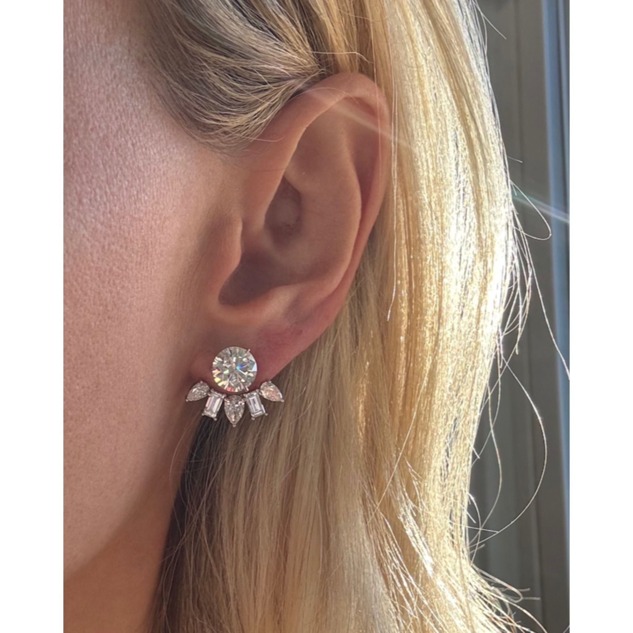 A close-up of a person’s ear with blonde hair wearing the Alternating Pear Shape and Emerald Cut Diamond Ear Jackets in 18K white gold, catching the sunlight.