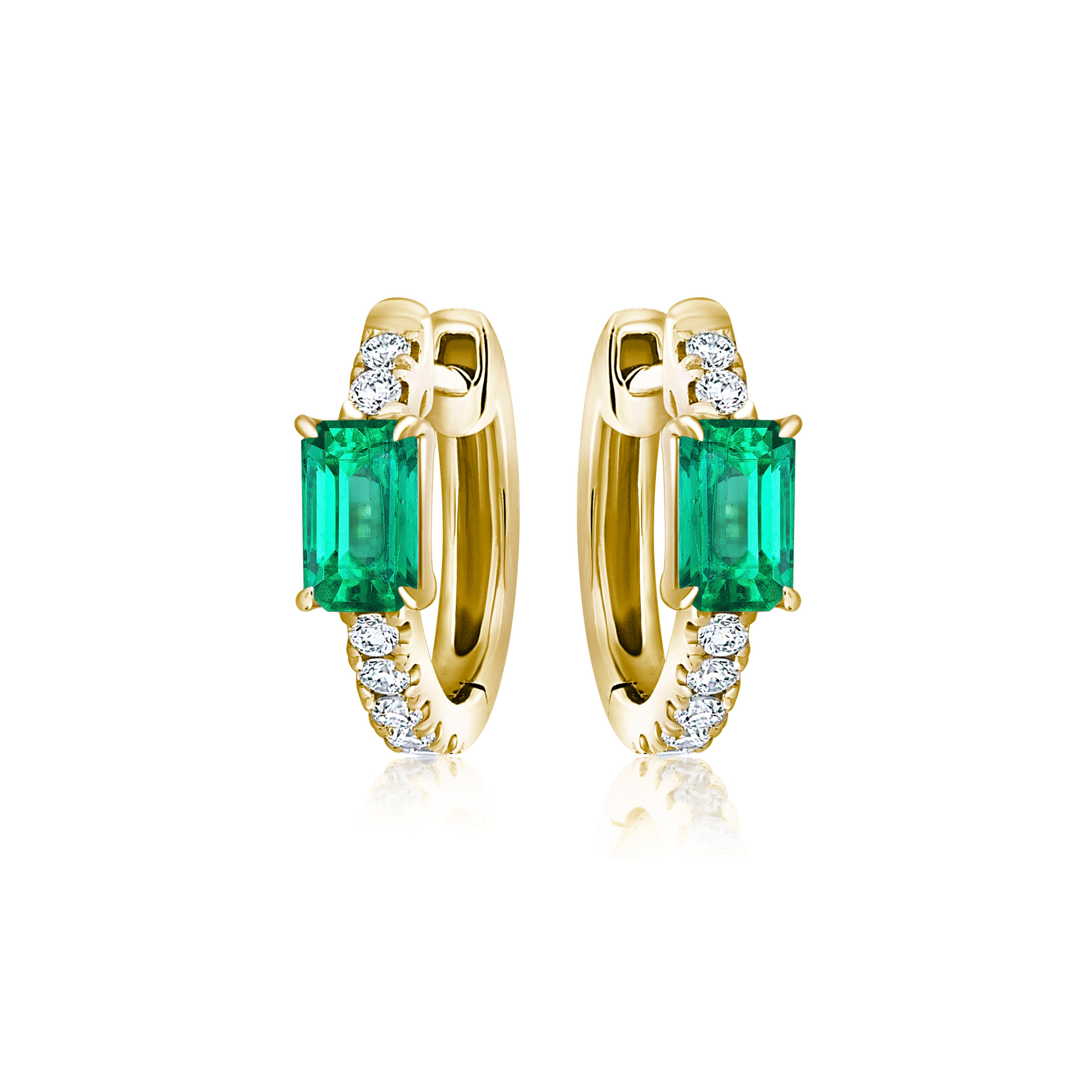 The Pavé Huggies in Yellow Gold with Emeralds are 18K gold hoop earrings, each showcasing an emerald cut emerald at the center and three white diamonds on either side, displayed against a white background.