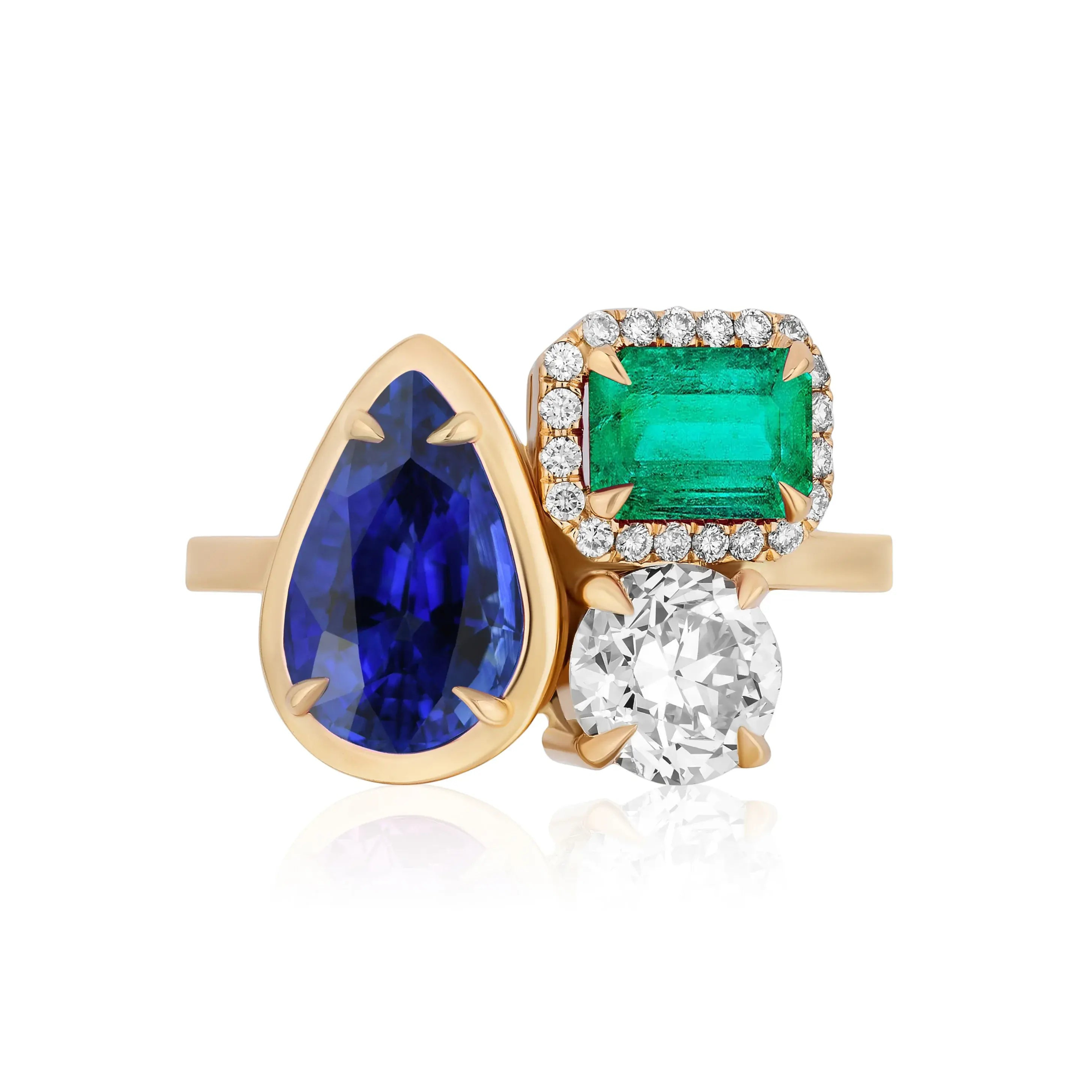 The Cluster Ring in yellow gold showcases a collet set pear shape sapphire, pavé emerald cut emerald, and round diamond, all set in elegant prongs.