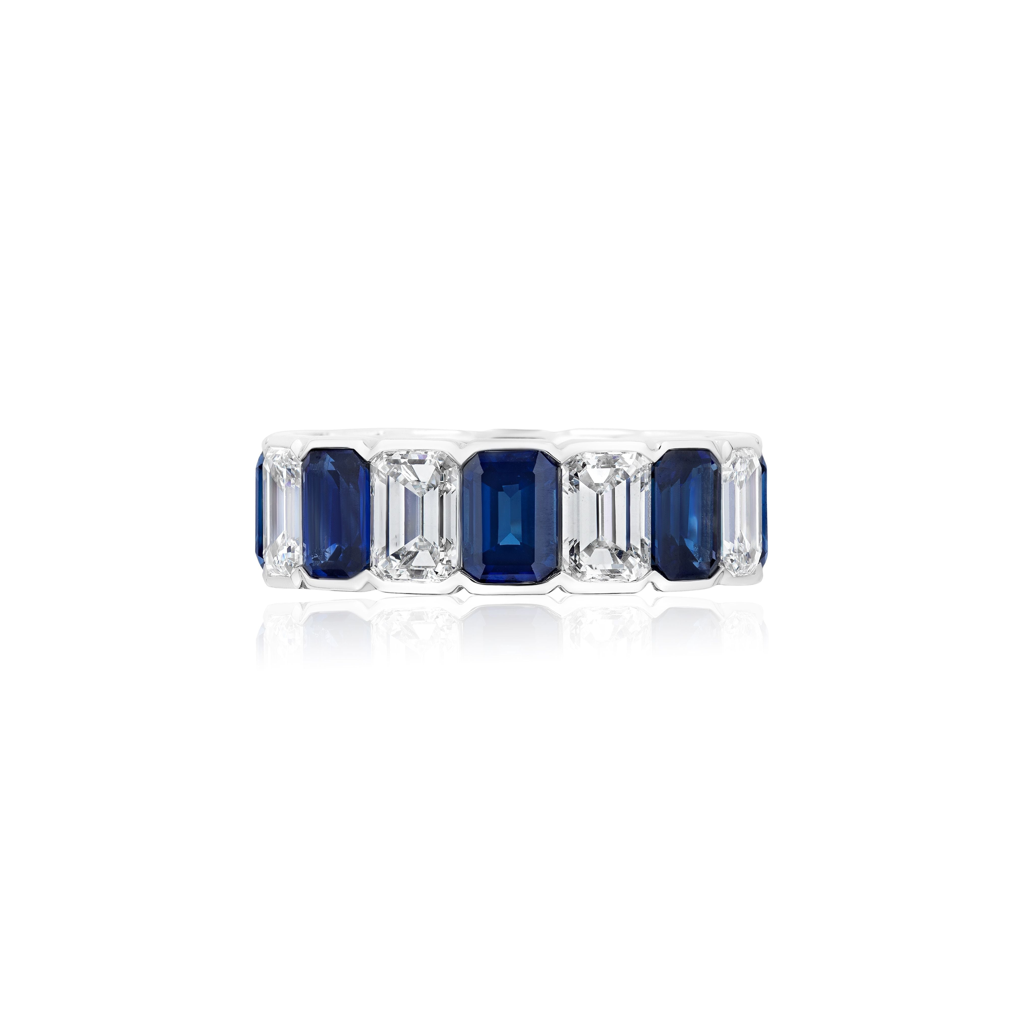 The Alternating Half-Bezel Emerald Cut Diamond and Sapphire Eternity Band, crafted in white gold, features a pattern of emerald-cut blue sapphires and white diamonds, showcased on a white background.