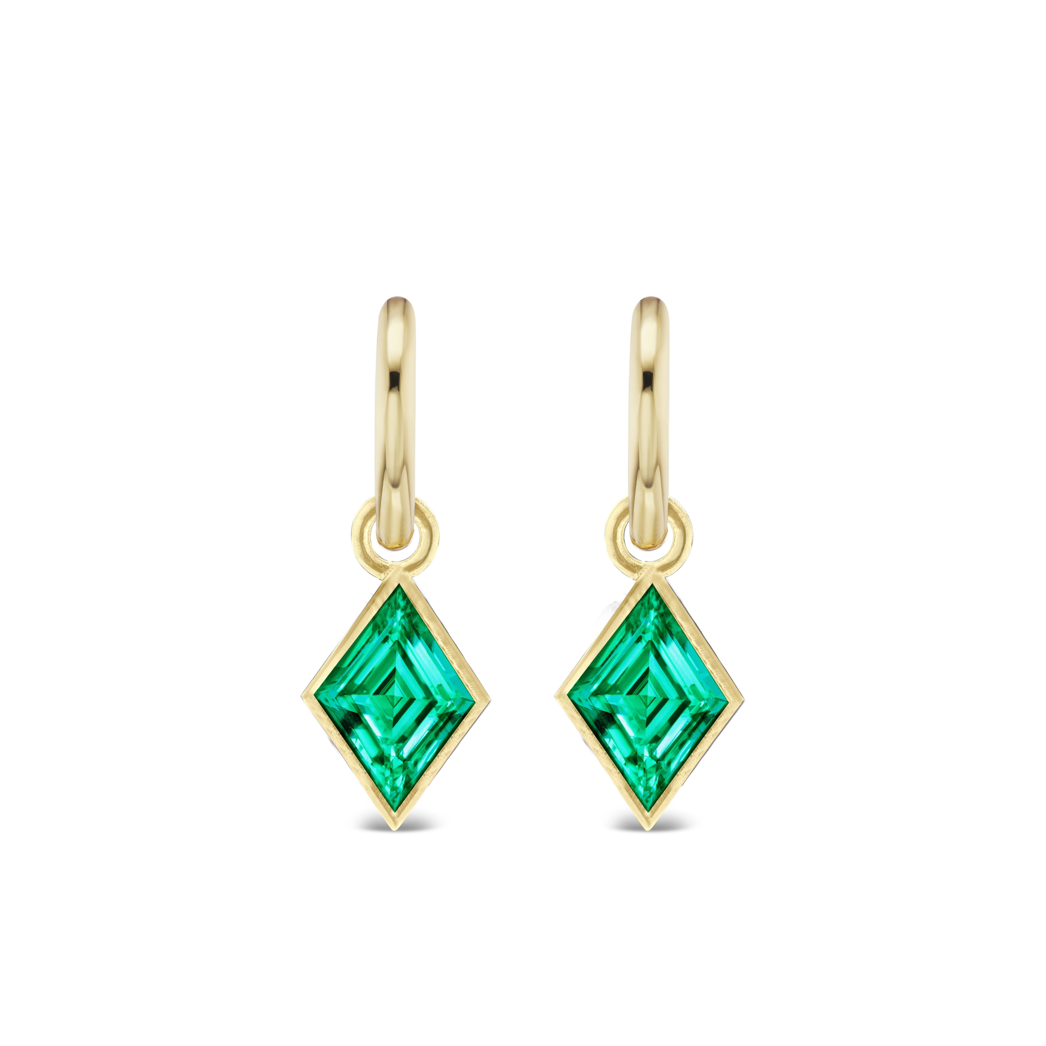 Huggies with bezel set kite shape emeralds, crafted from 18K yellow gold, are displayed on a white background.