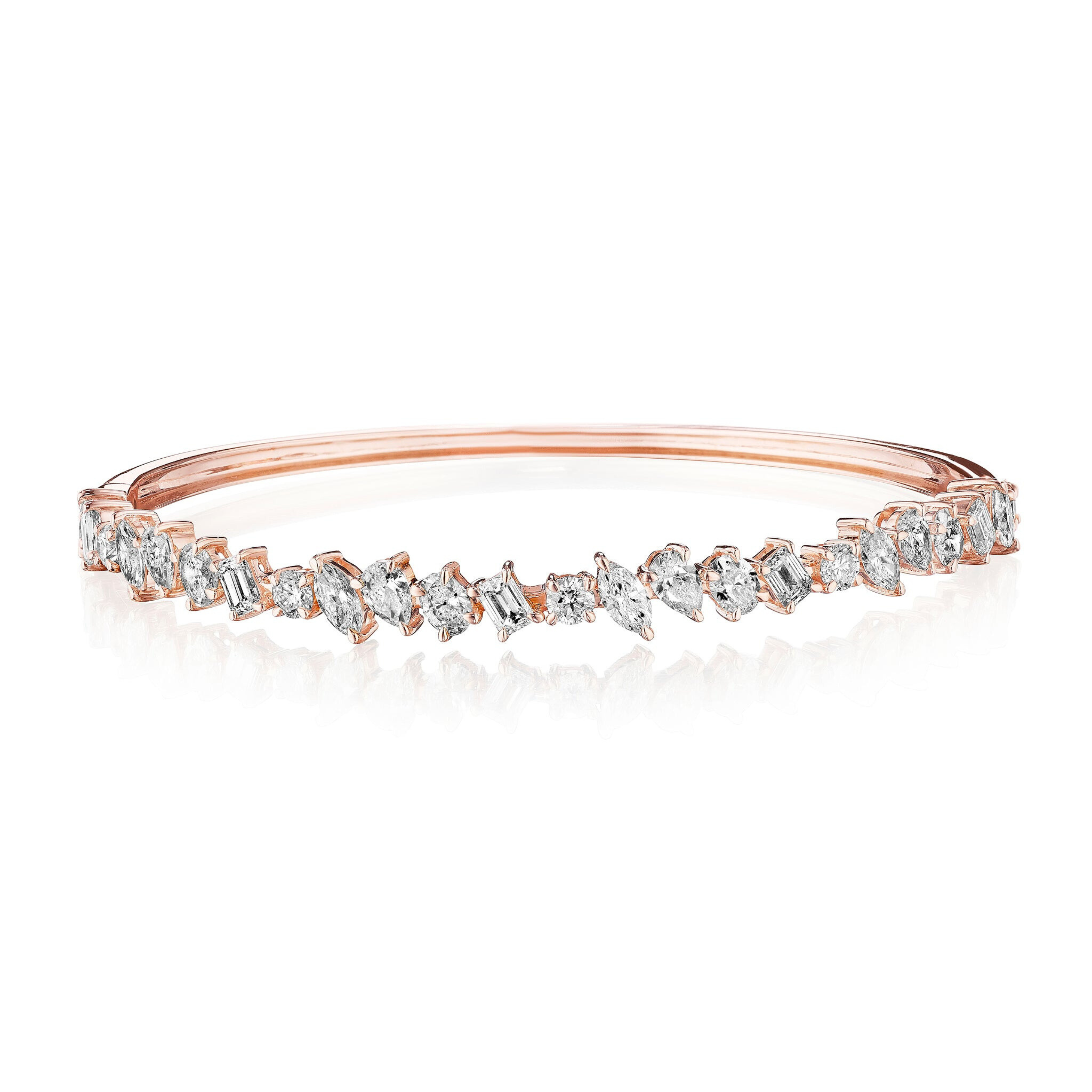 The Marching Mixed Shape Diamond Bangle, crafted in 18K rose gold with clear gemstones and emerald cut diamonds in an irregular pattern, showcases a sparkling, elegant design against a white background.
