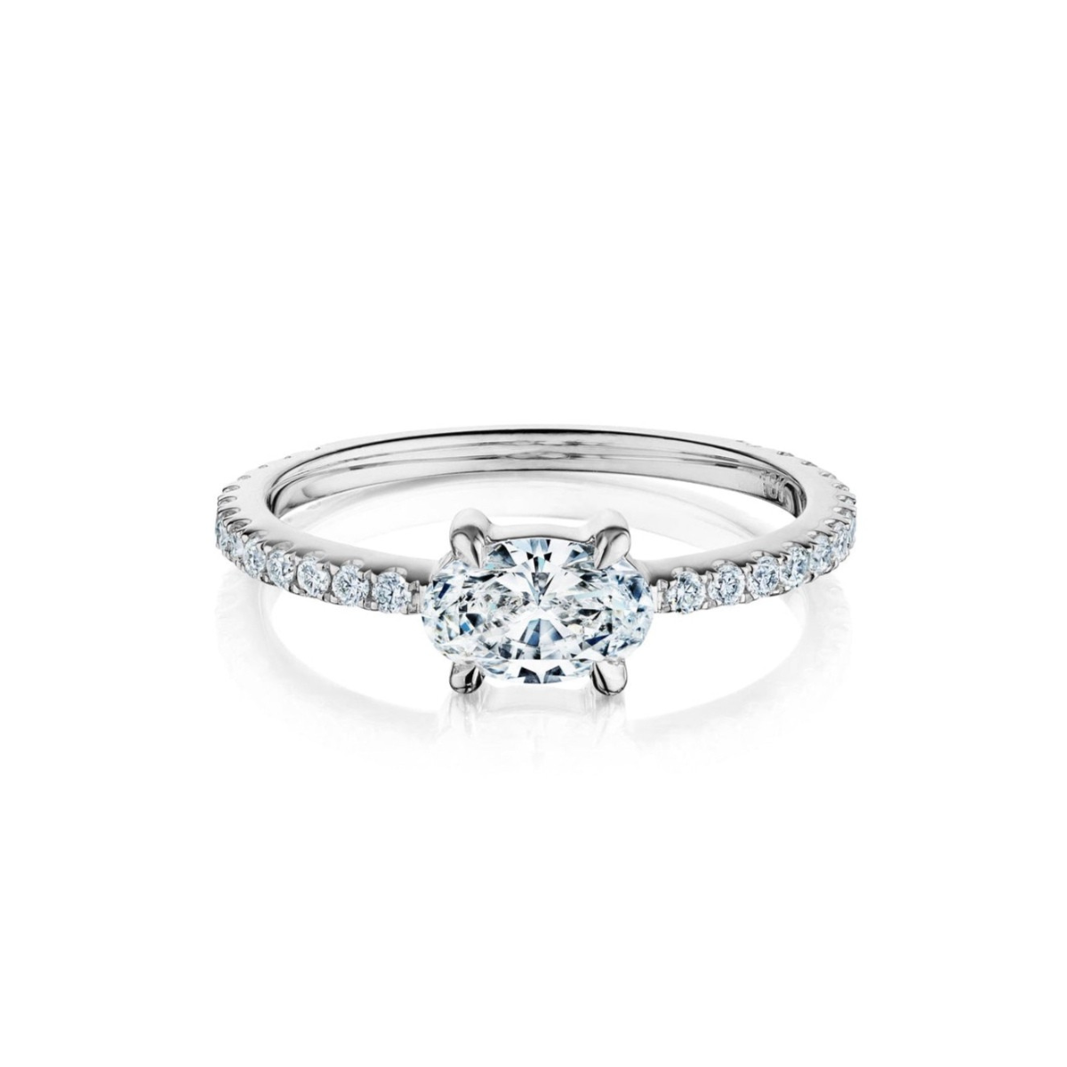 The East-West Set Oval Diamond Ring with Pavé Band in White Gold features an oval-cut center diamond and pavé-set round diamonds, beautifully displayed on a white background.