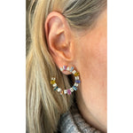 Close-up of a woman with light blonde hair in a gray knit sweater wearing Confetti Front-to-Back Hoops featuring emerald cut diamonds and multicolor sapphires set in 18K yellow gold.