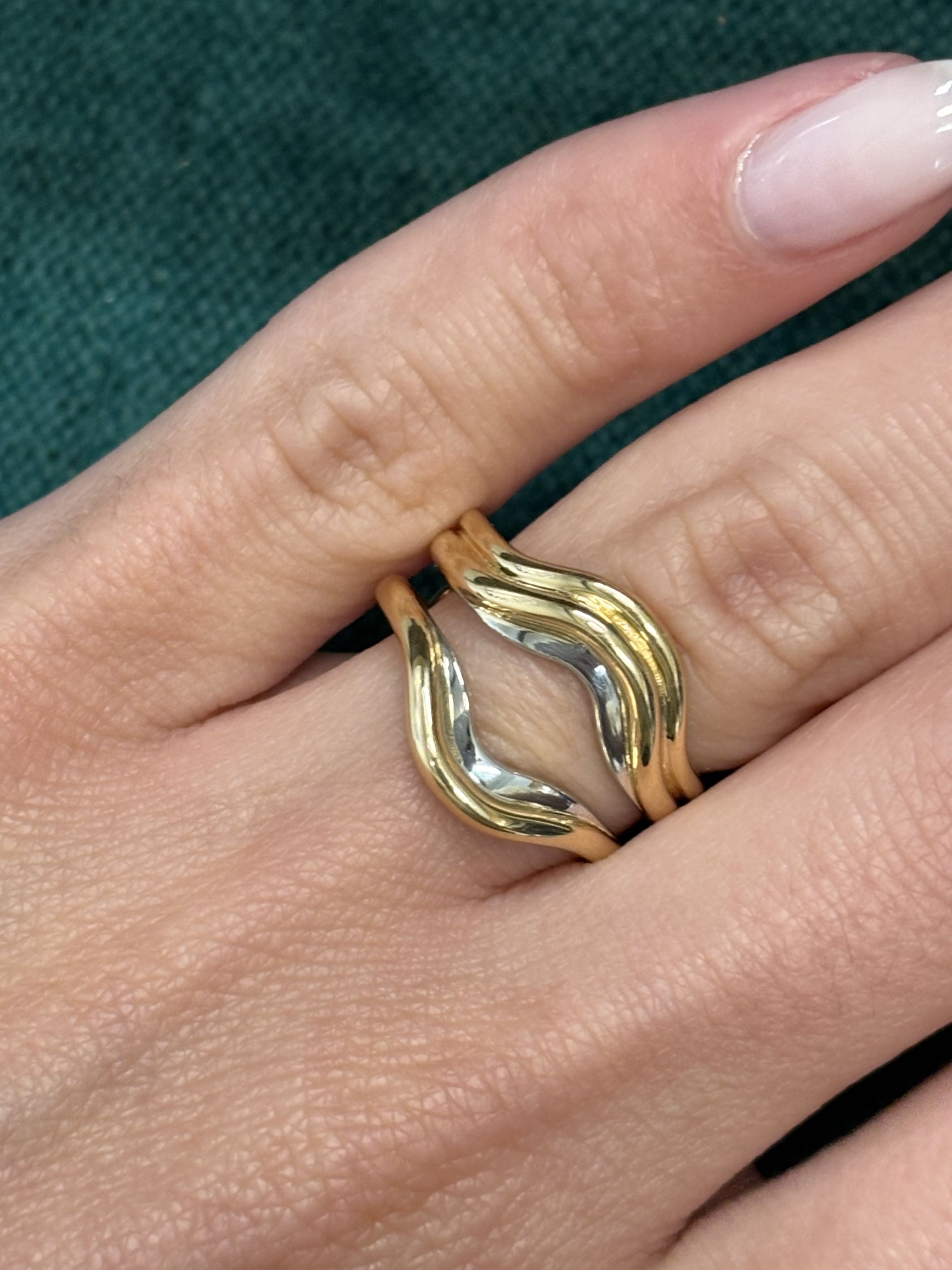 A close-up shows a hand wearing the Single and Double Band Contour Ring Jacket in Yellow Gold on the middle finger, with wavy yellow gold and silver bands fitting together like a puzzle against textured dark green fabric.