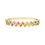 The Chroma Chevron Bezel Set Multicolor Baguette Sapphire Bangle in Yellow Gold features a zigzag pattern of square settings with vibrant blue, purple, pink, orange, and yellow sapphires, shown on a white background.