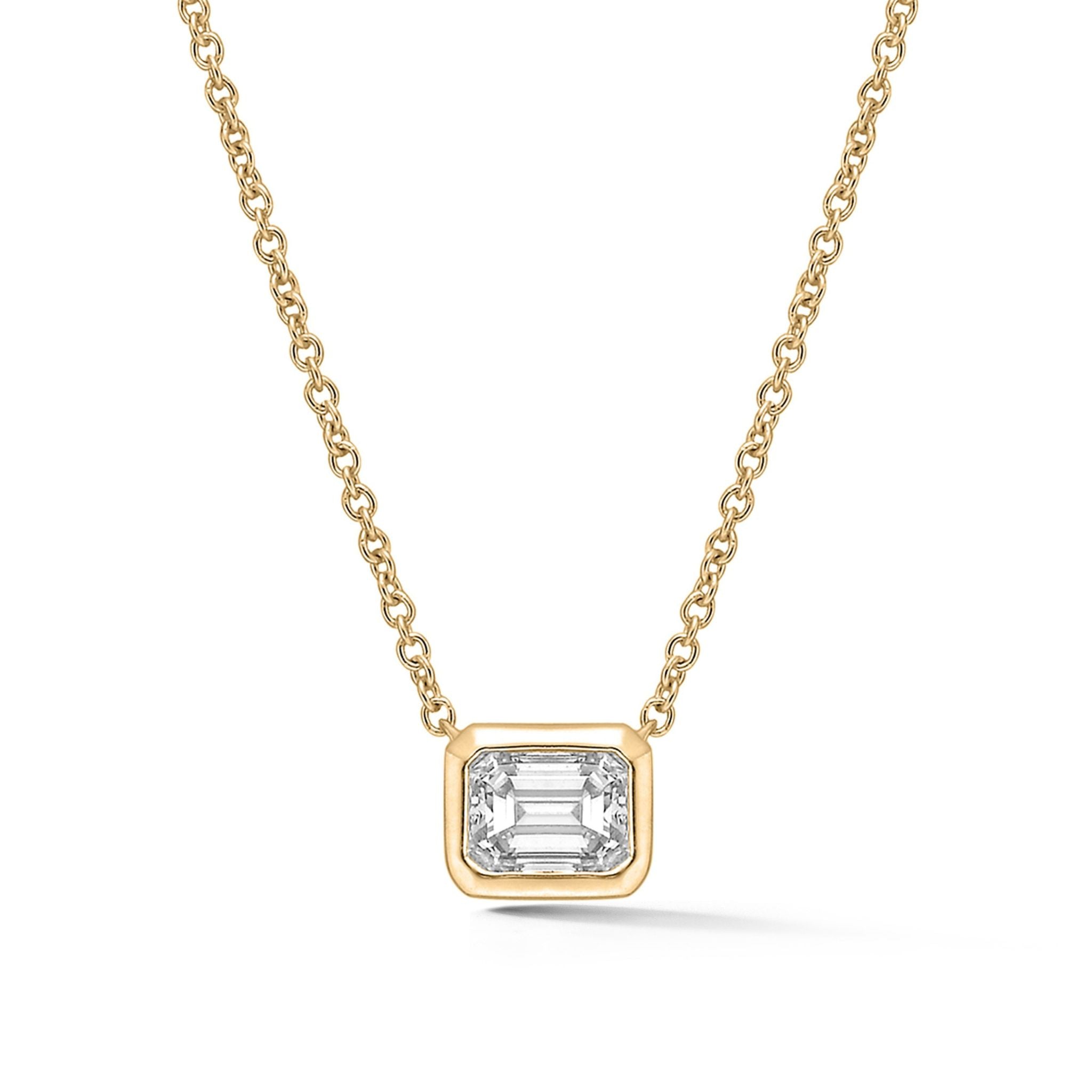 The Bezel Set Emerald Cut Diamond Solitaire Pendant in Yellow Gold features a timeless emerald cut diamond set in a simple 18K yellow gold bezel.