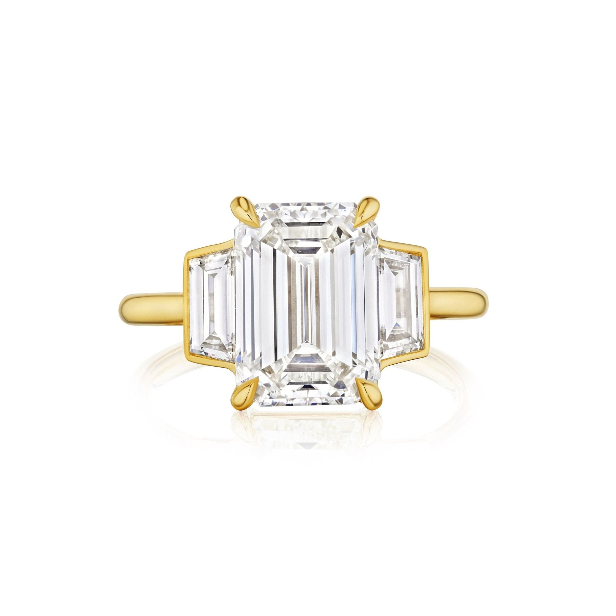 The Emerald Cut Diamond Engagement Ring with Trapezoid Side Stones features an emerald cut diamond center, two trapezoid diamonds on each side, and a minimal 18k yellow gold setting with clean, modern lines.