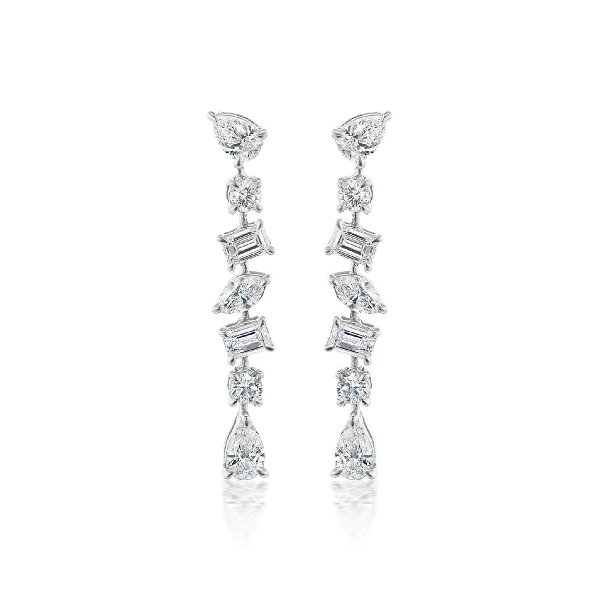The Tennis Drop Earrings in White Gold with Mixed Shape Diamonds feature round, pear, and rectangular diamonds arranged vertically in an elegant 18K white gold setting.