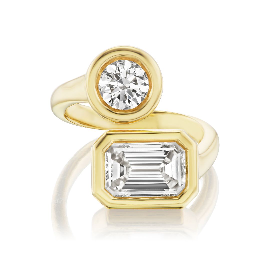 The Toi Et Moi Wraparound Ring features bezel-set round and emerald cut diamonds totaling 3.95 tcw in 18K yellow gold, with an open bypass design for a modern, elegant look.
