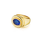 The 1970s Gold and Sapphire Ring features a thick gold band with an oval-shaped deep blue sapphire elegantly set at its center, displayed in a classic gold mounting and photographed against a white background.